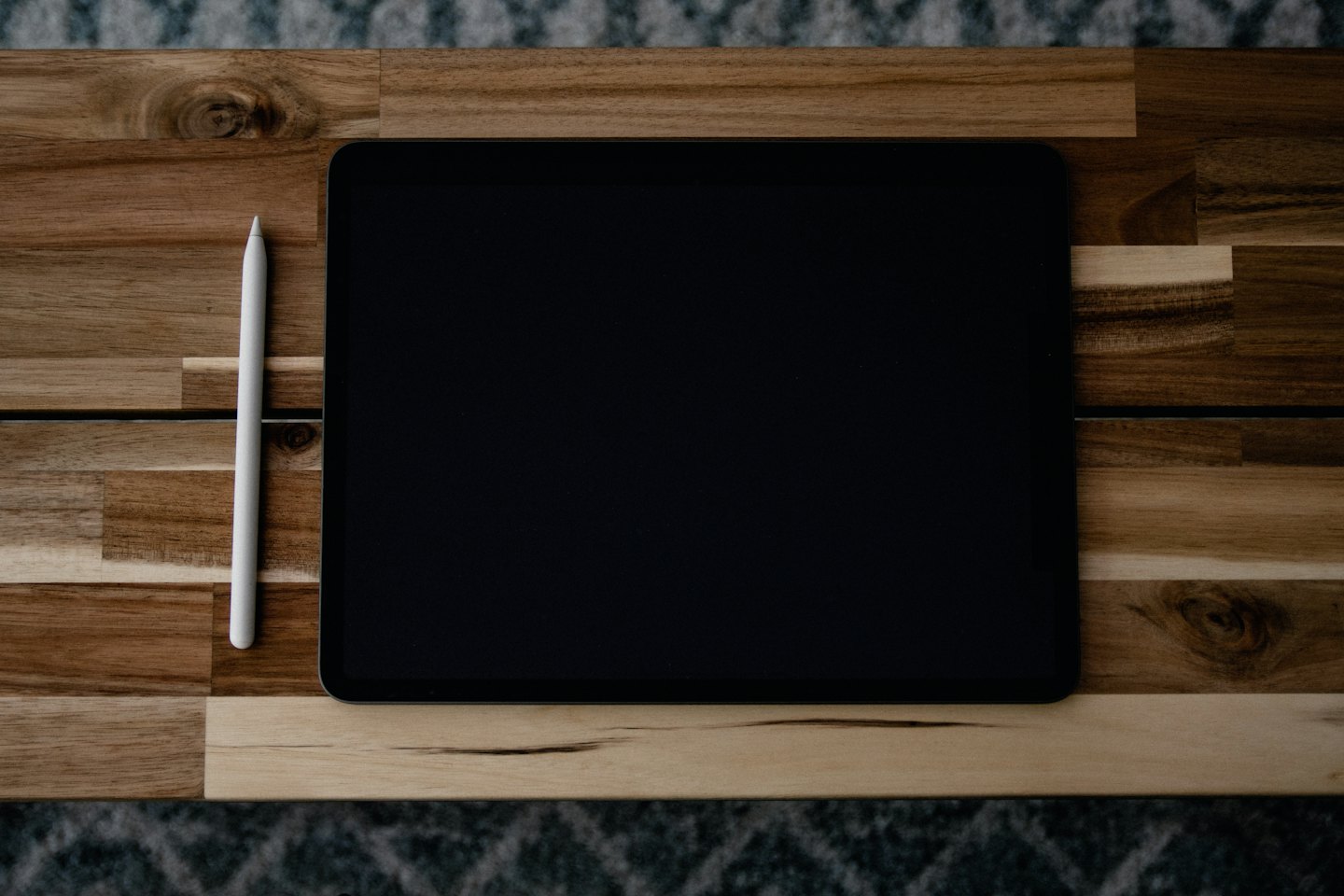 Tablet and stylus on a wooden desk with rug.