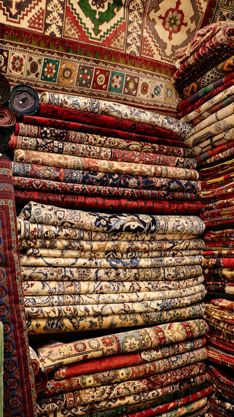 Stacks of colorful oriental rugs with intricate patterns and fringes.