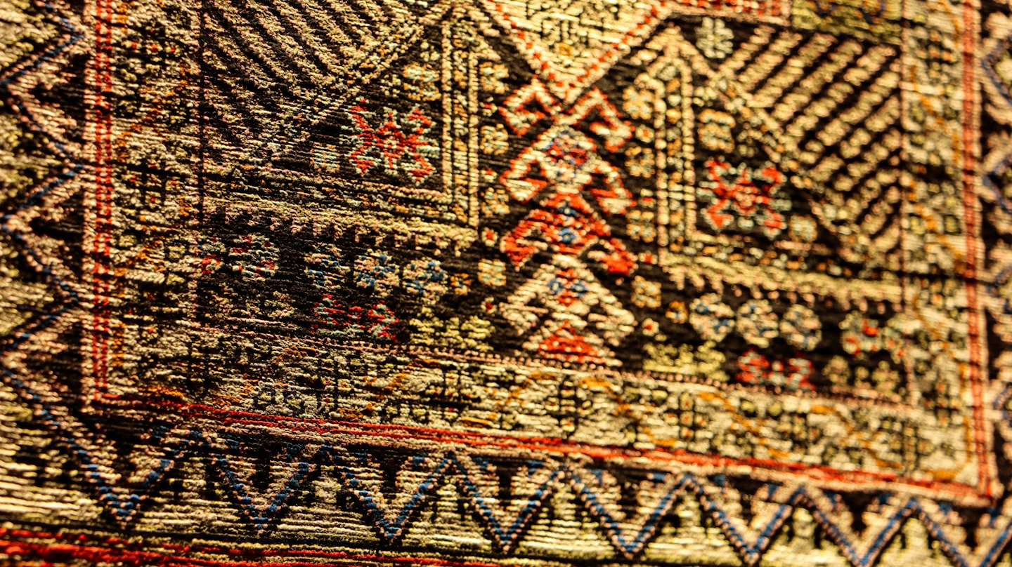 Intricate geometric and floral patterns woven into a colorful rug.
